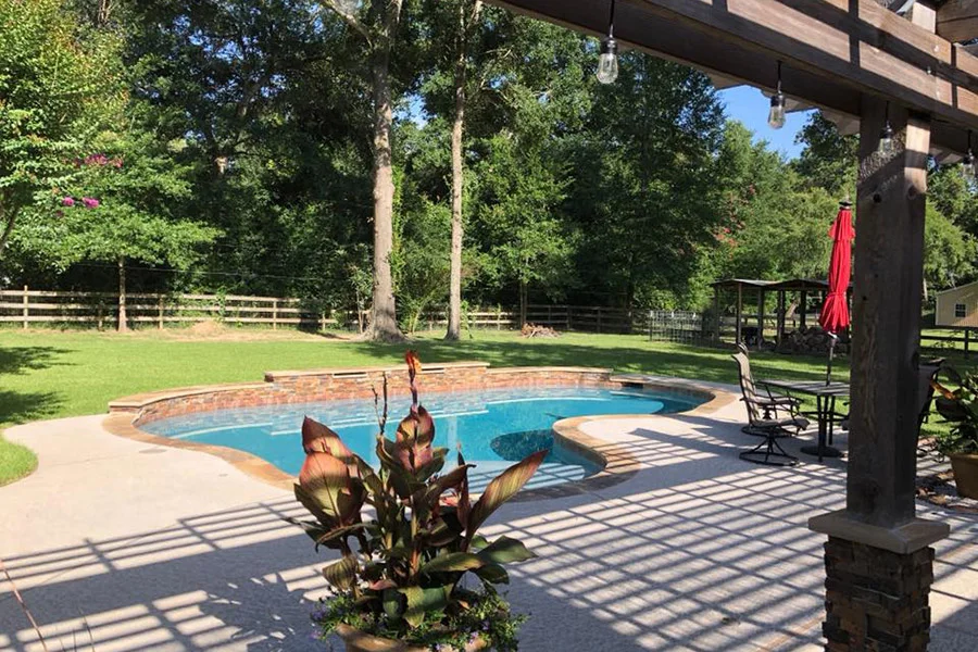 happy family enjoying BBQ next to crystal-clear custom gunite pool in flat sunny Houston backyard - cost of custom pools